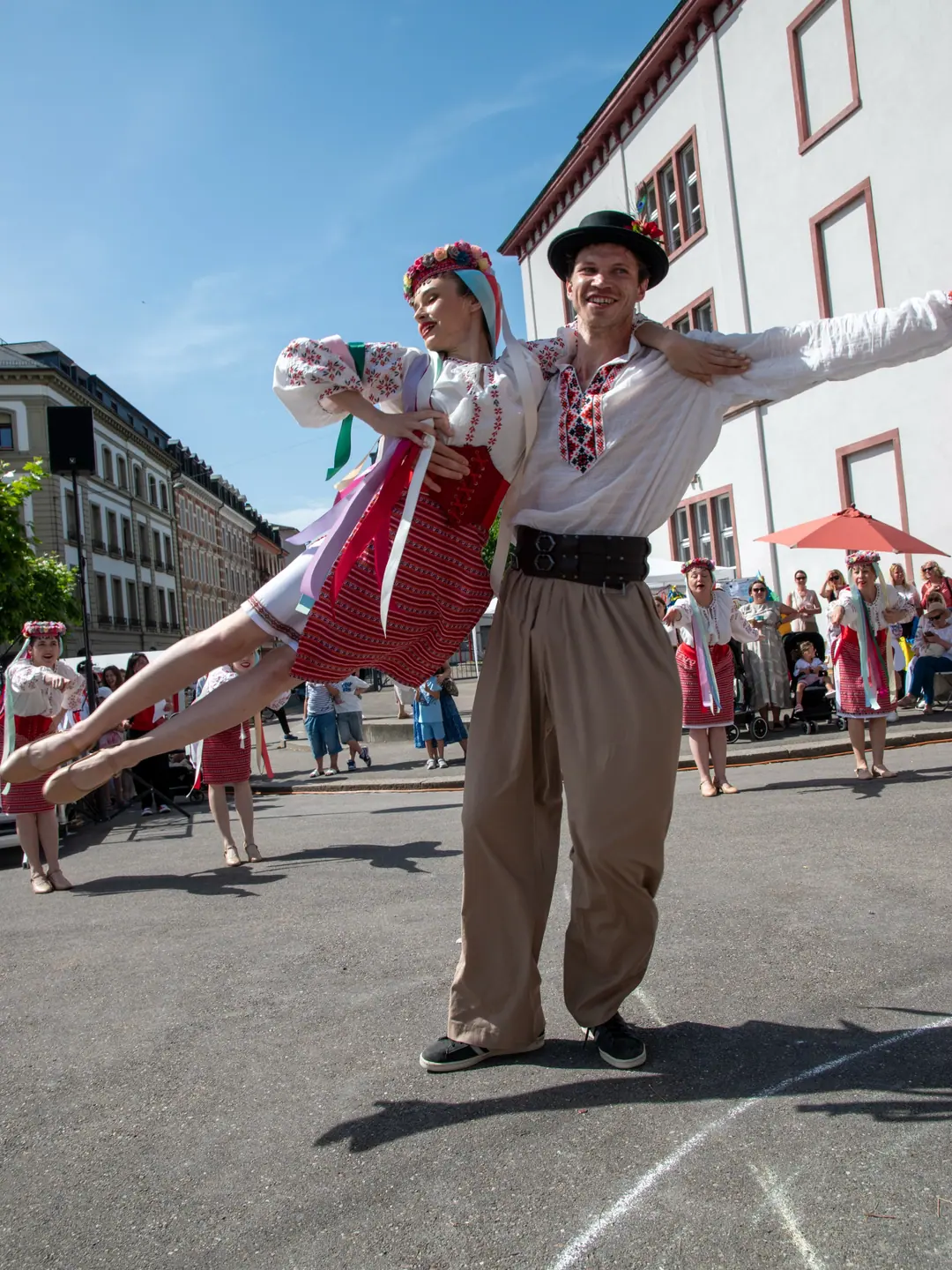 Ein Tänzer hebt seine Partnerin hoch über den Theodorskirchplatz, beide in ukrainischer Tracht
